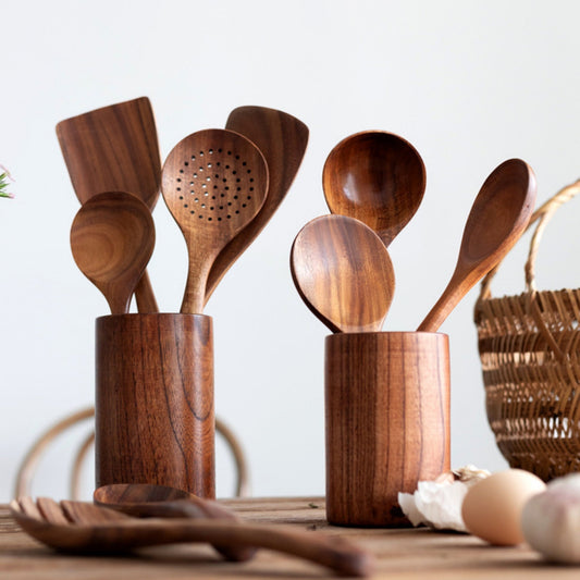 Teak wood cooking utensils including spoons and spatulas in matching wooden holders on kitchen table